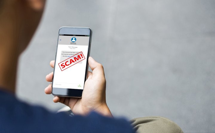 Tangan memegang ponsel yang menampilkan pesan penipuan bertanda SCAM